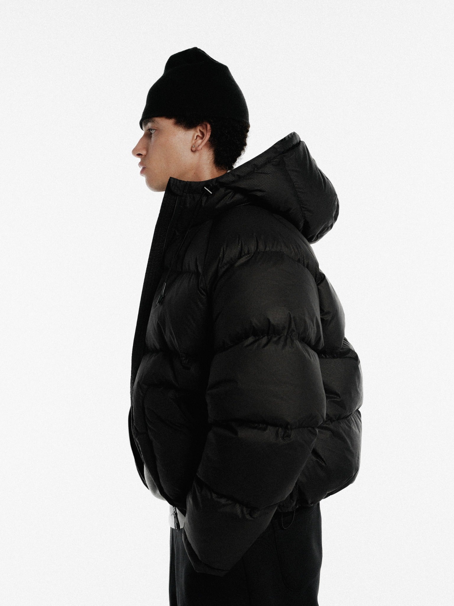 Black hooded puffer jacket by Sweats UK, shown in a close-up image highlighting its quilted design and padded warmth.
