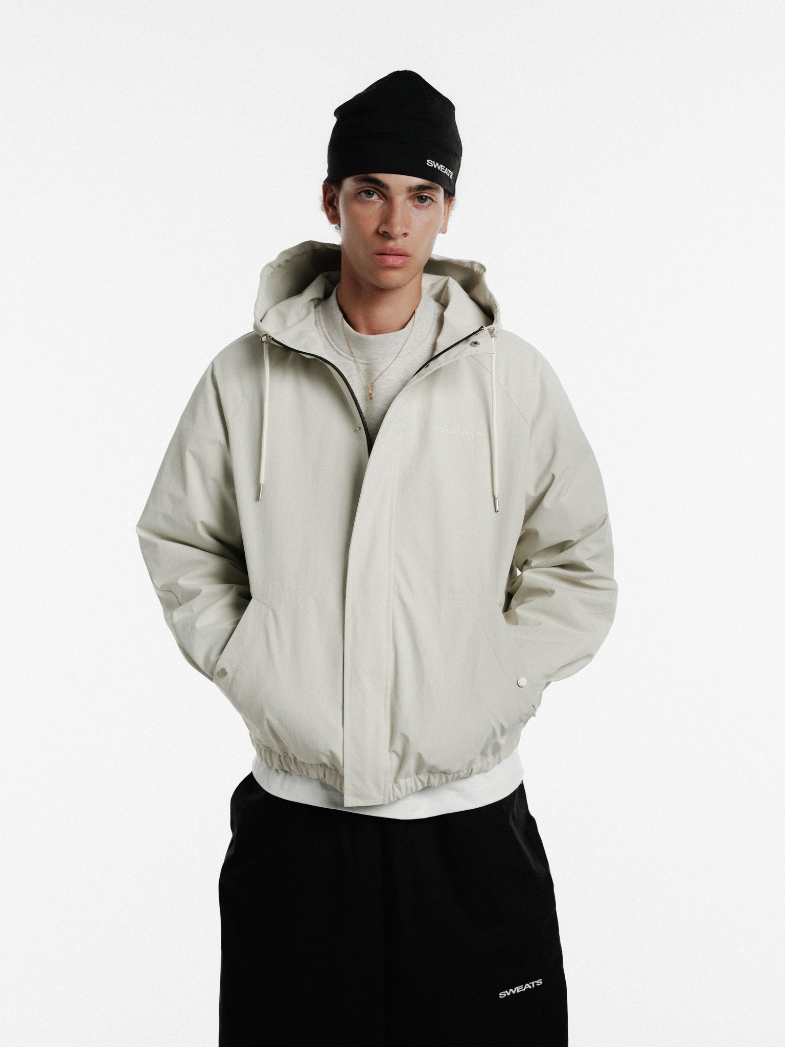 Stone-colored ARC JACKET by Sweats UK, showcasing a stylish winter jacket with a hood and zipper closure.