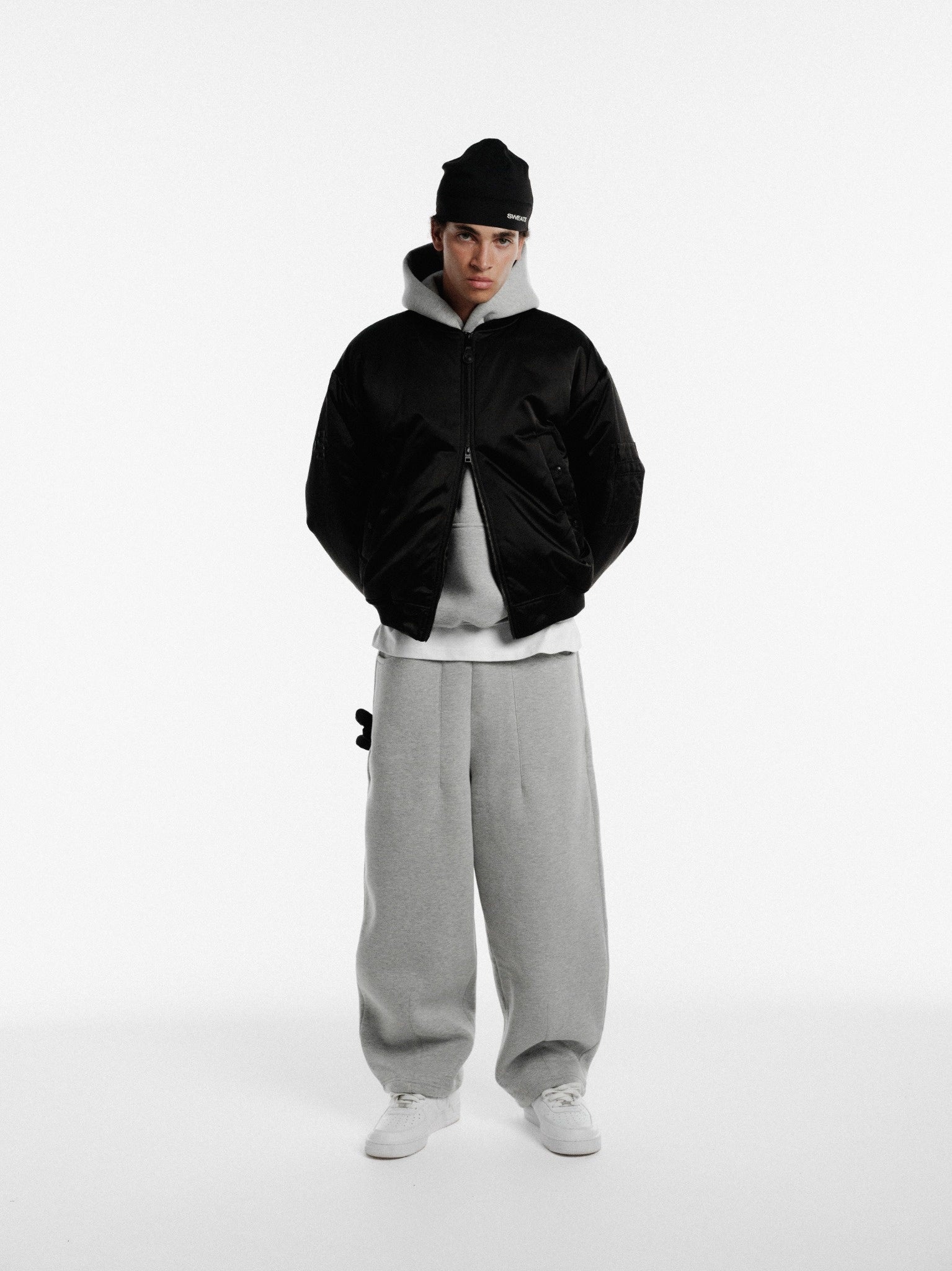 Black bomber jacket by Sweats UK, shown on model, with front zipper and ribbed cuffs, stylish winter outerwear.
