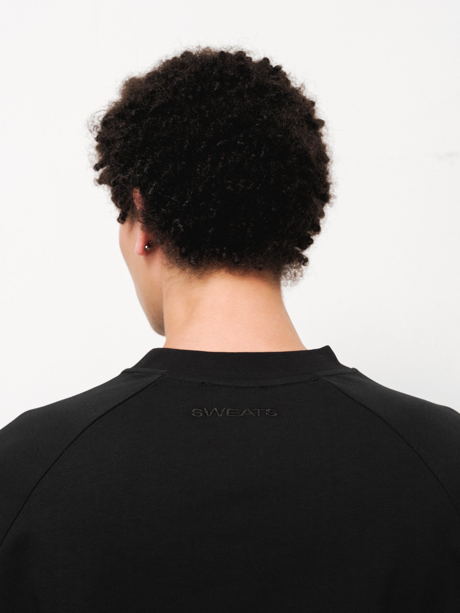 Black long sleeve T-shirt by Sweats UK displayed on a model, showing a casual fit and simple design.