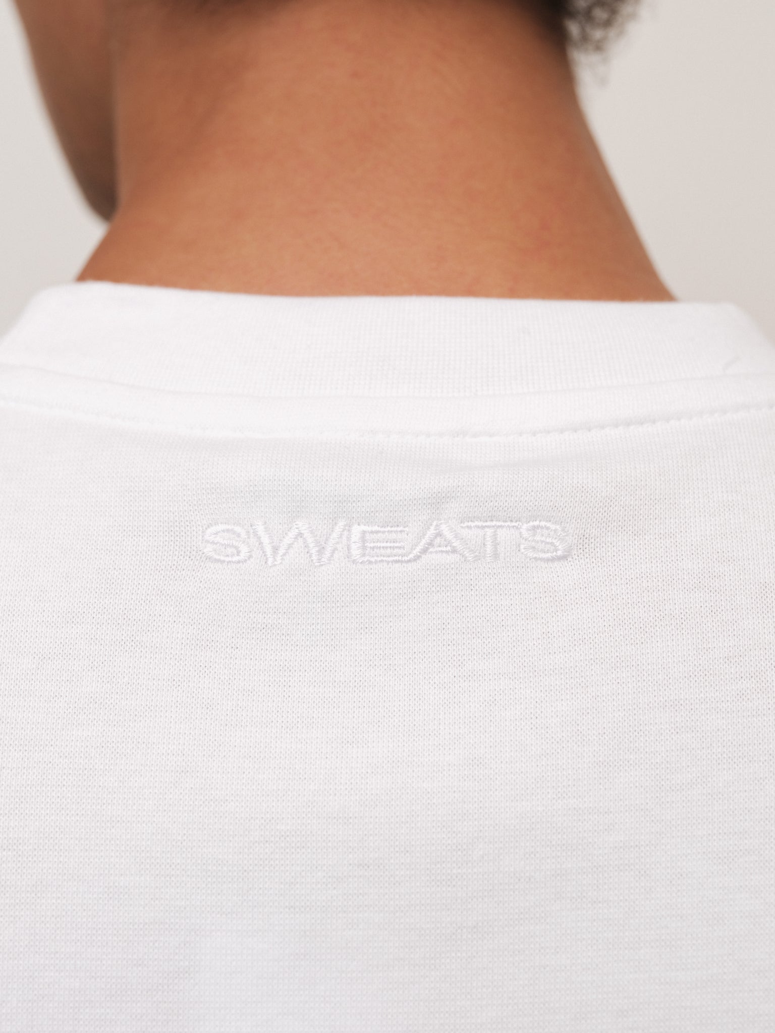 White fitted T-shirt from Sweats UK shown on model, featuring a classic crew neck and short sleeves.