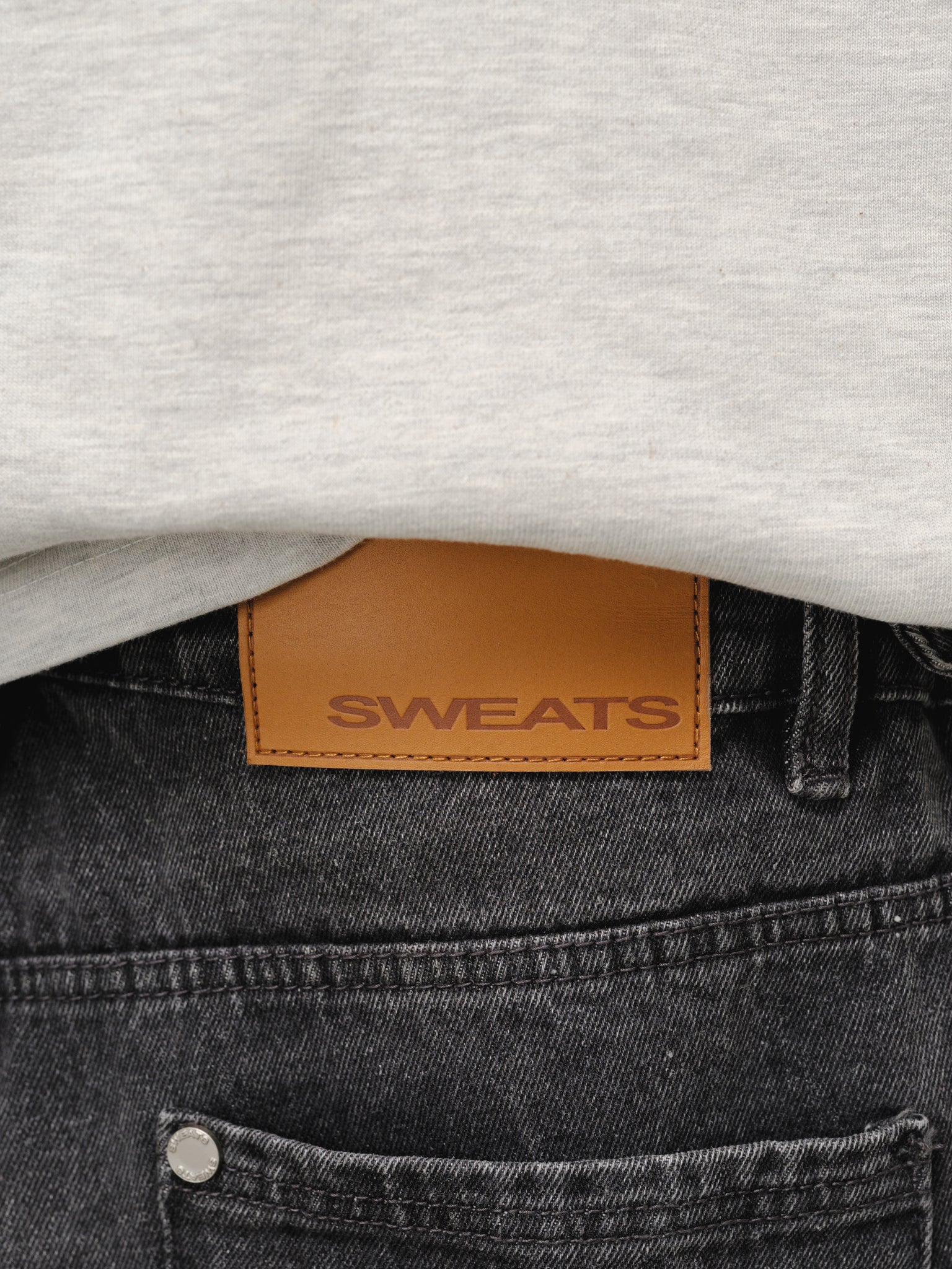 Sweats UK washed black denim baggy jeans displayed on a hanger, showcasing relaxed fit and stylish casual design.